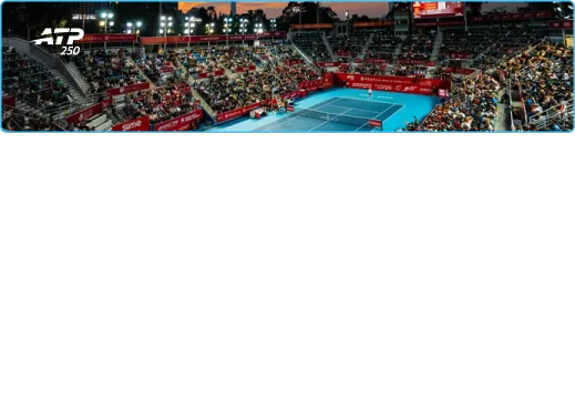 Stade de tennis bondé au crépuscule, éclairé par des lumières vives pour l'événement ATP 250. Des banderoles rouges vives entourent le court bleu, créant une atmosphère énergique.